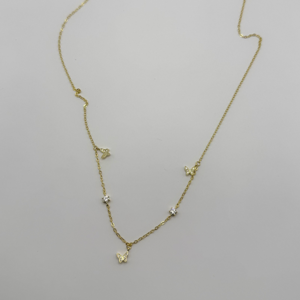 A delicate gold chain necklace with small butterfly and star charms, displayed on a plain white surface.