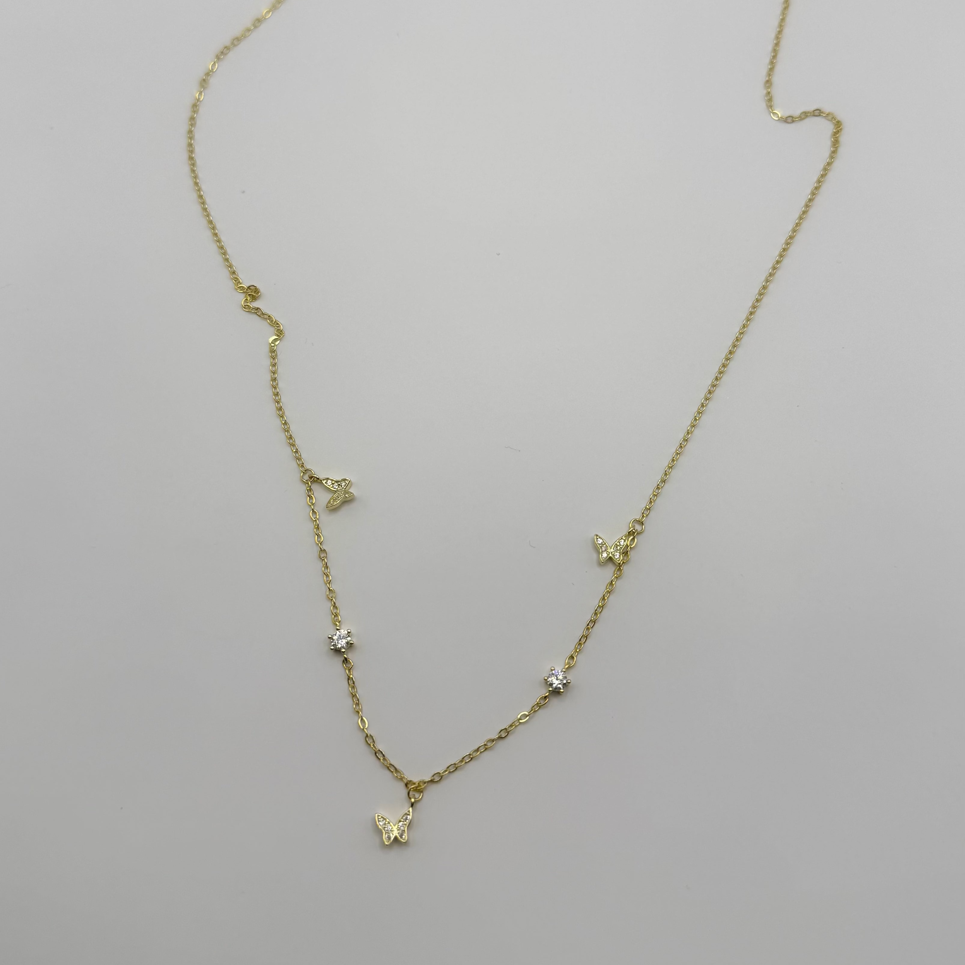 A delicate gold chain necklace with small butterfly and star charms, displayed on a plain white surface.
