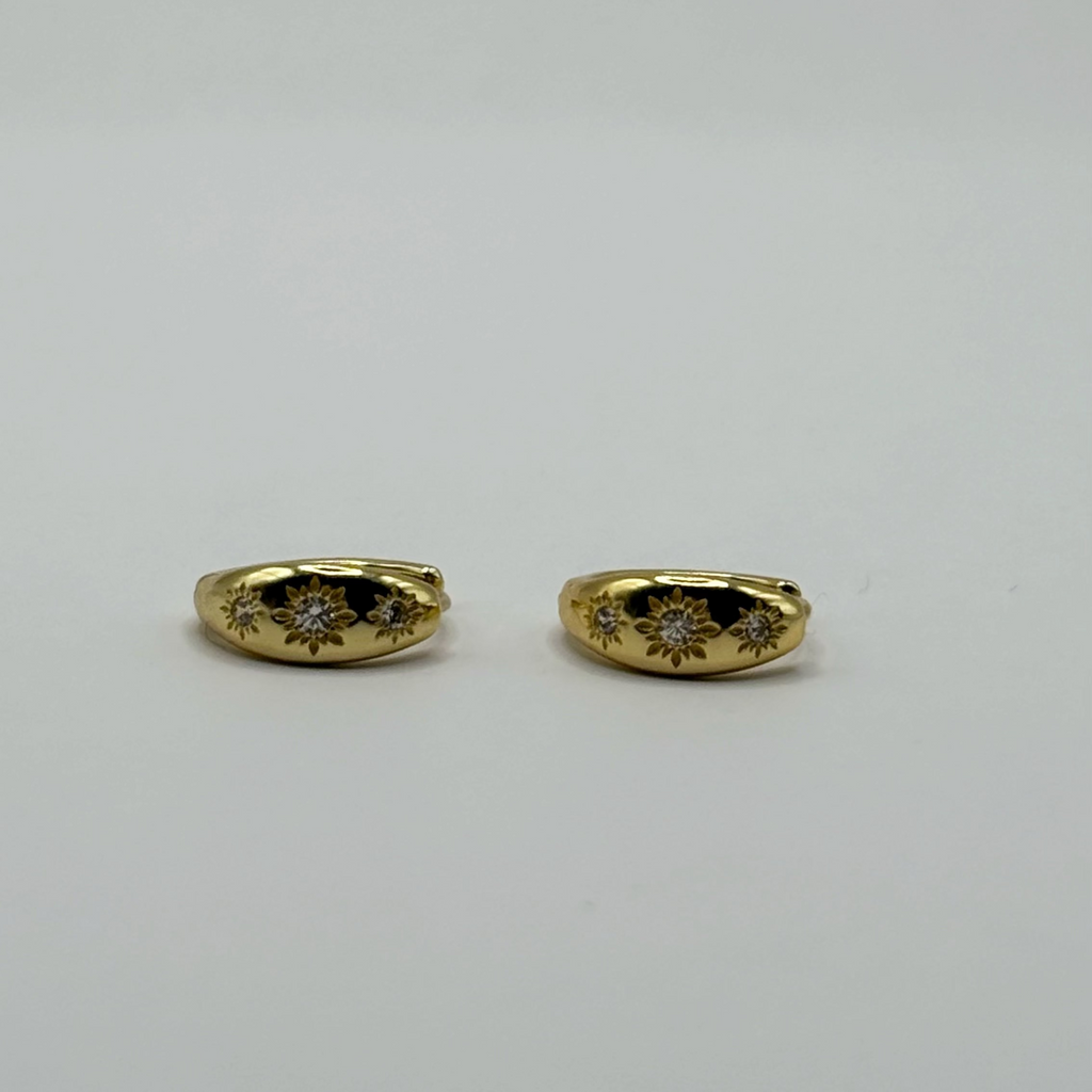 A pair of gold hoop earrings with diamond floral engravings, displayed on a neutral white background.