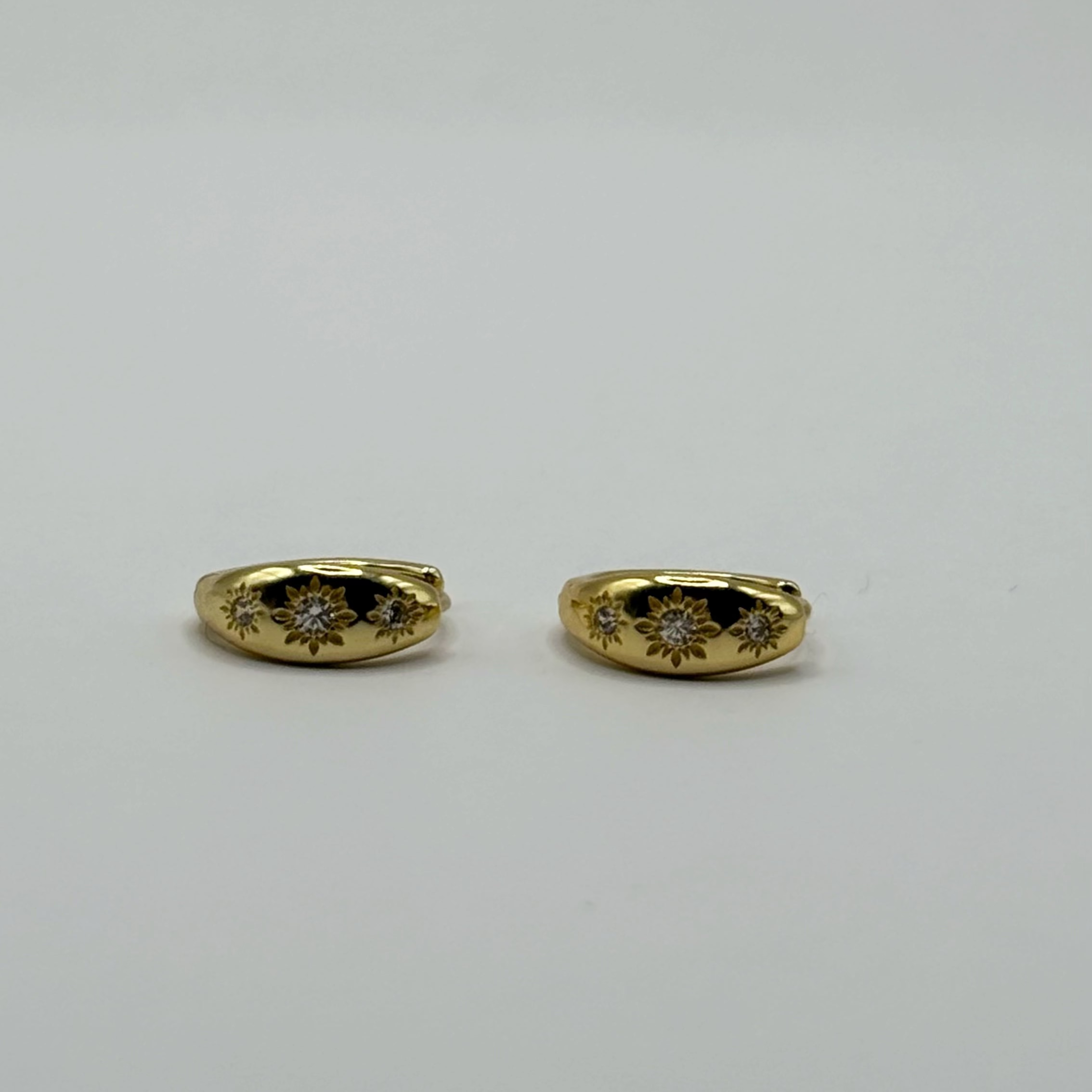 A pair of gold hoop earrings with diamond floral engravings, displayed on a neutral white background.